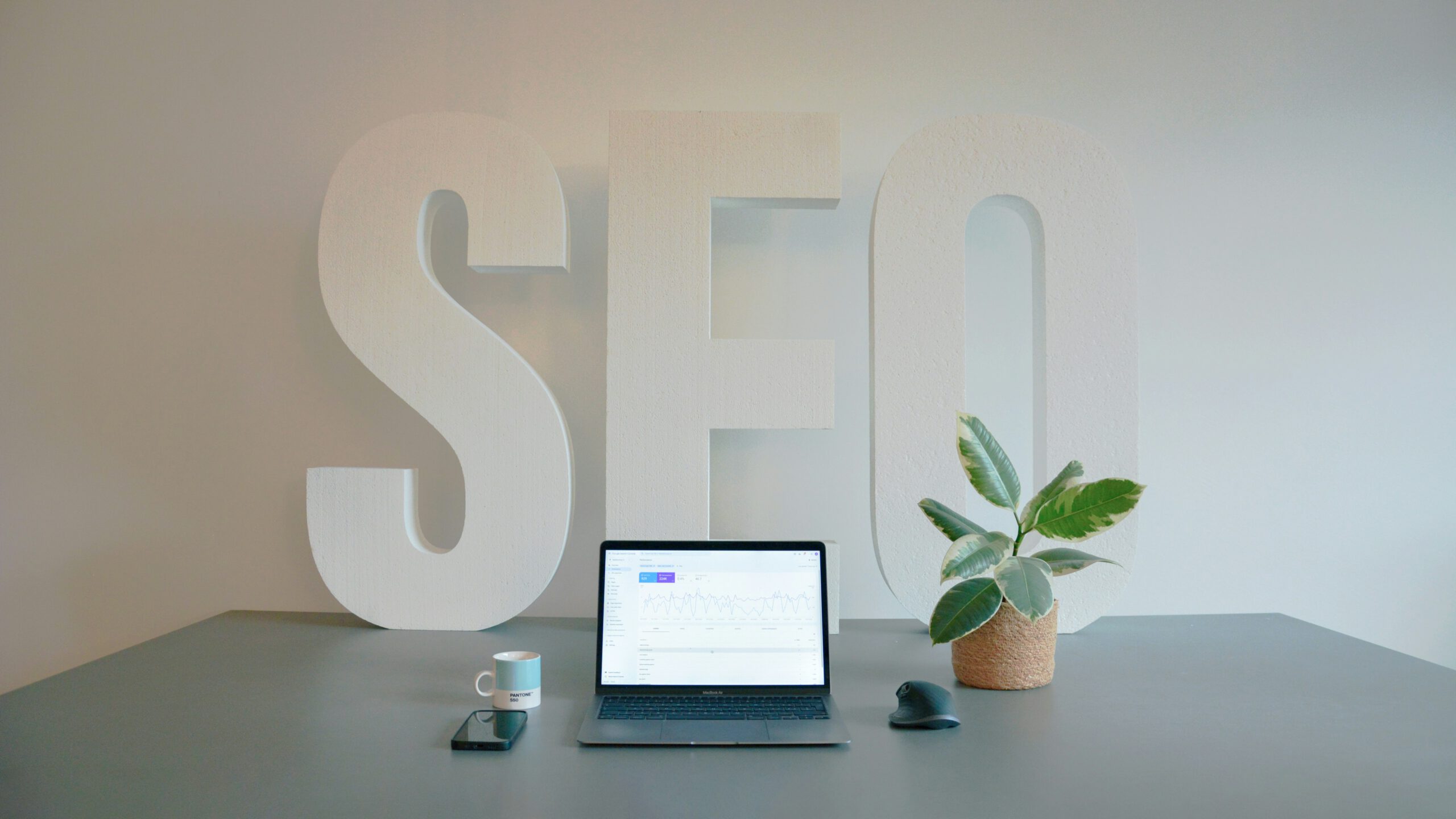 GEO en SEO analyse op bureau met laptop, plant en grote SEO letters op de achtergrond